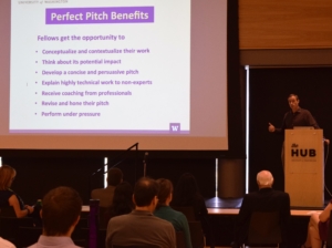A Rad Roberts stands at a podium next to a sign listing the benefits of the Perfect Pitch session. Photo, Robin Brooks, eScience Institute